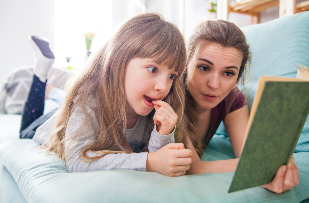 Mother and daughter sitting on sofa at home and reading book together